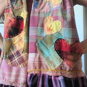 May include: A patchwork scarf and vest combination in a variety of plaid patterns. The scarf and vest feature appliqued heart shapes in various colors. The bottom of the vest has a ruffled hem. The color palette includes pink, red, yellow, blue, and green.