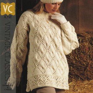 Puede incluir: Un suéter de punto blanco con un patrón de diamantes y cables de encaje. El suéter tiene cuello alto y mangas largas. El suéter se muestra en una modelo que lleva un gorro y guantes blancos. El texto "VC Knit Vintage Classics Lacy Diamonds & Cables" es visible en el lado izquierdo de la imagen.