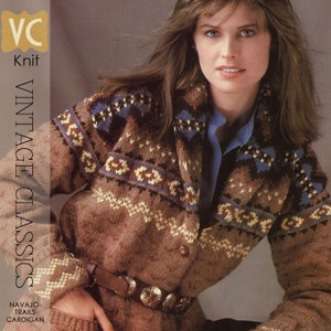 May include: A brown knitted cardigan with a colourful geometric pattern. The cardigan has a shawl collar and a button closure. The model is wearing a blue shirt underneath the cardigan.