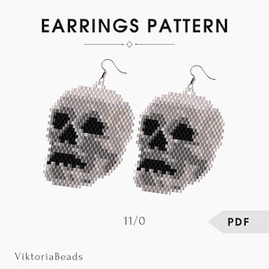 Op de afbeelding: Een paar schedelvormige oorbellen gemaakt van kleine, lichtgrijze en zwarte kralen. De oorbellen hebben een haaksluiting en zijn voorzien van het label "EARNINGS PATTERN" met de tekst "11/0" en "PDF". De merknaam "ViktoriaBeads" is ook zichtbaar.