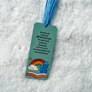 May include: A blue bookmark with a quote from Roald Dahl: "and above all, watch with glittering eyes the whole world around you, because the greatest secrets are always hidden in the most unusual places". The bookmark features a colourful illustration of a book, rainbow, and clouds.