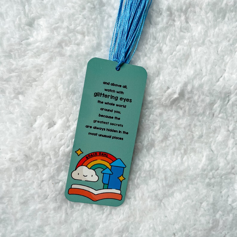 May include: A blue bookmark with a quote from Roald Dahl: "and above all, watch with glittering eyes the whole world around you, because the greatest secrets are always hidden in the most unusual places". The bookmark features a colourful illustration of a book, rainbow, and clouds.