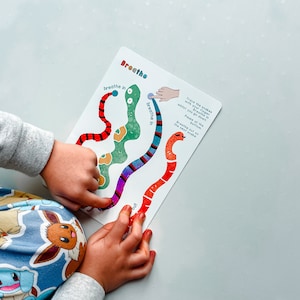 Puede incluir: Una tarjeta colorida con un dise&ntilde;o de serpiente roja, verde y azul. La tarjeta tiene las palabras "Inhala" y "Exhala" escritas en ella. La tarjeta est&aacute; siendo utilizada por un ni&ntilde;o para practicar ejercicios de respiraci&oacute;n.