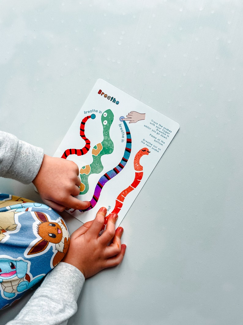Puede incluir: Una tarjeta colorida con un dise&ntilde;o de serpiente roja, verde y azul. La tarjeta tiene las palabras "Inhala" y "Exhala" escritas en ella. La tarjeta est&aacute; siendo utilizada por un ni&ntilde;o para practicar ejercicios de respiraci&oacute;n.
