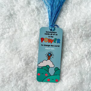 May include: Blue bookmark with a quote from Roald Dahl: "Somewhere inside all of us is the power to change the world." The bookmark features a cartoon illustration of a hand reaching up to a star.
