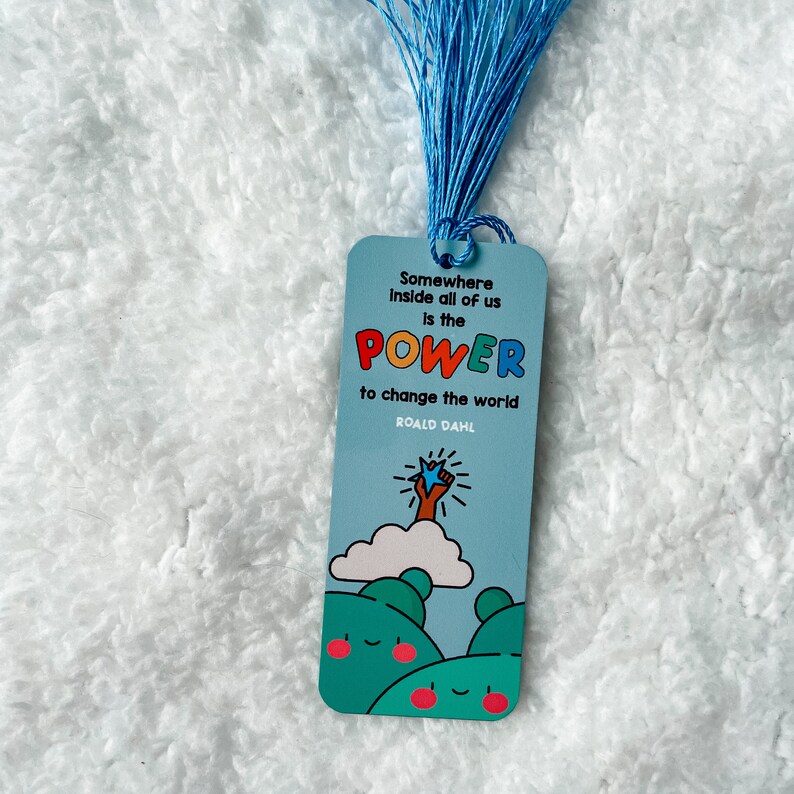 May include: Blue bookmark with a quote from Roald Dahl: "Somewhere inside all of us is the power to change the world." The bookmark features a cartoon illustration of a hand reaching up to a star.
