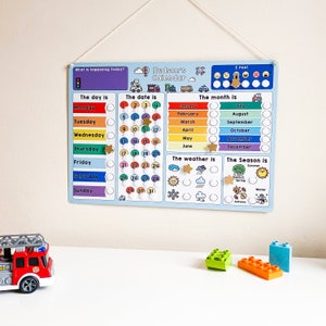 K&ouml;nnte beinhalten: Ein blauer und wei&szlig;er Kinderkalender mit einem farbenfrohen Regenbogen-Design. Der Kalender enth&auml;lt Wochentage, Daten, Monate, Wetter und Jahreszeiten. Der Kalender tr&auml;gt den Titel "Hudsons Kalender".