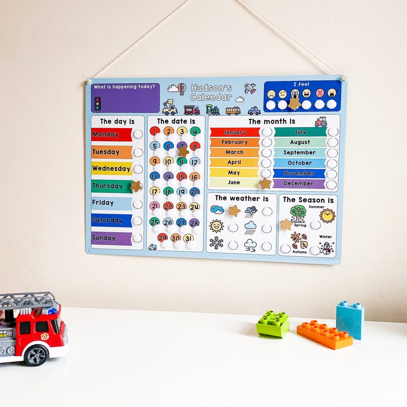 K&ouml;nnte beinhalten: Ein blauer und wei&szlig;er Kinderkalender mit einem farbenfrohen Regenbogen-Design. Der Kalender enth&auml;lt Wochentage, Daten, Monate, Wetter und Jahreszeiten. Der Kalender tr&auml;gt den Titel "Hudsons Kalender".