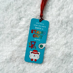 May include: Blue bookmark with a red string attached. The bookmark features a cat with a red hat and the text "why fit in, when you were born to STAND OUT DR. SEUSS".