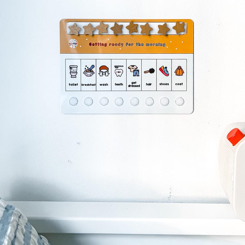 May include: A white and orange morning routine chart with wooden star-shaped magnets. The chart includes illustrated icons for tasks like toilet, breakfast, and getting dressed. The text "Getting ready for the morning" is printed on the chart.