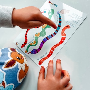 Puede incluir: Una tarjeta colorida con un dise&ntilde;o de serpiente. La tarjeta tiene las palabras "inspirar" y "expirar" escritas en ella. La mano de un ni&ntilde;o est&aacute; trazando la serpiente con su dedo.