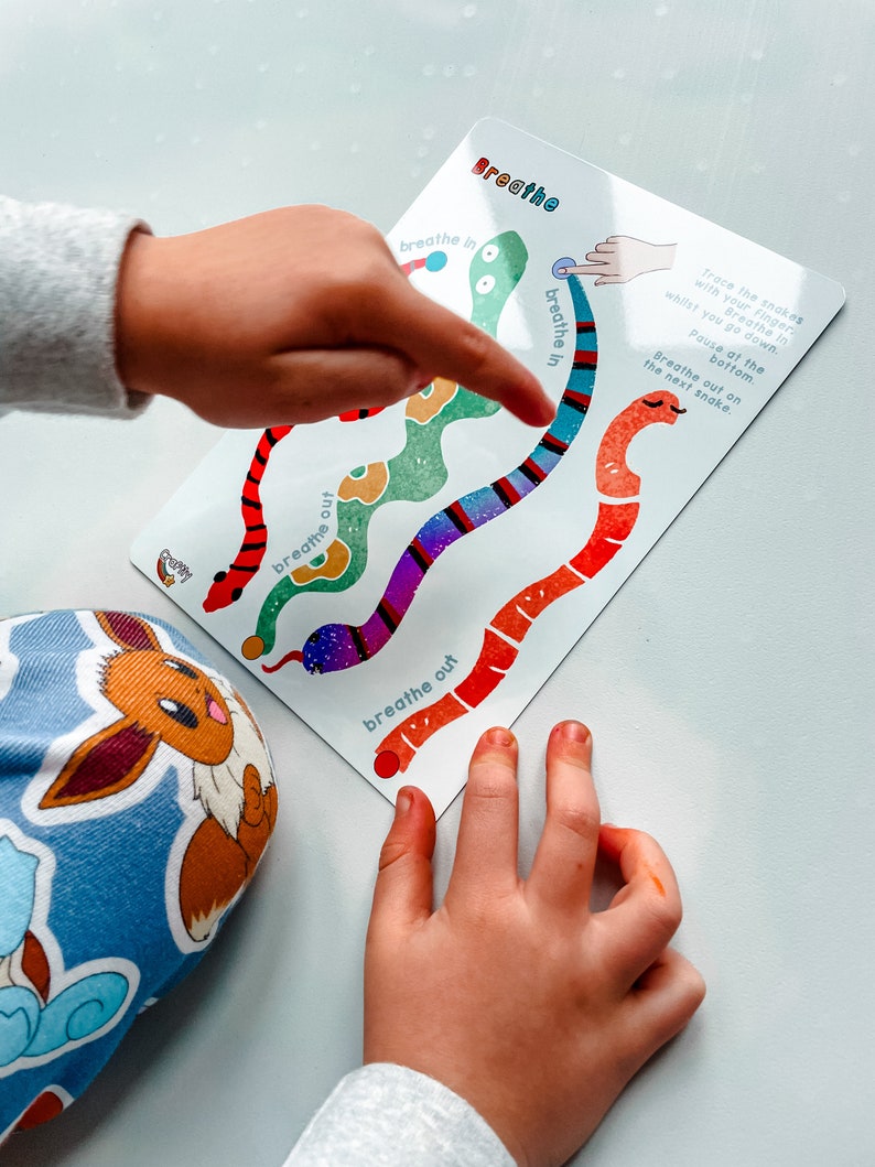 Puede incluir: Una tarjeta colorida con un dise&ntilde;o de serpiente. La tarjeta tiene las palabras "inspirar" y "expirar" escritas en ella. La mano de un ni&ntilde;o est&aacute; trazando la serpiente con su dedo.