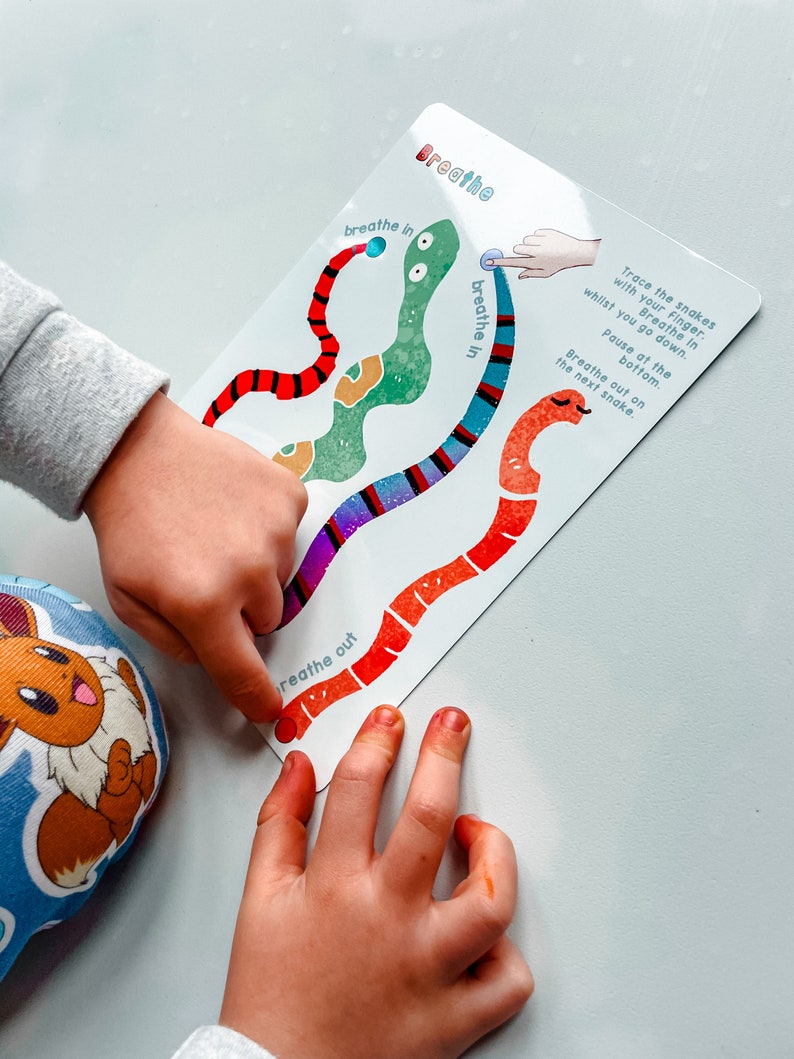 Puede incluir: Un juego de aprendizaje colorido con un fondo blanco y la palabra "Breathe" en la parte superior. El juego presenta tres serpientes con rayas de diferentes colores y las palabras "breathe in" y "breathe out" escritas en ellas. El juego est&aacute; dise&ntilde;ado para ayudar a los ni&ntilde;os a aprender sobre la respiraci&oacute;n.