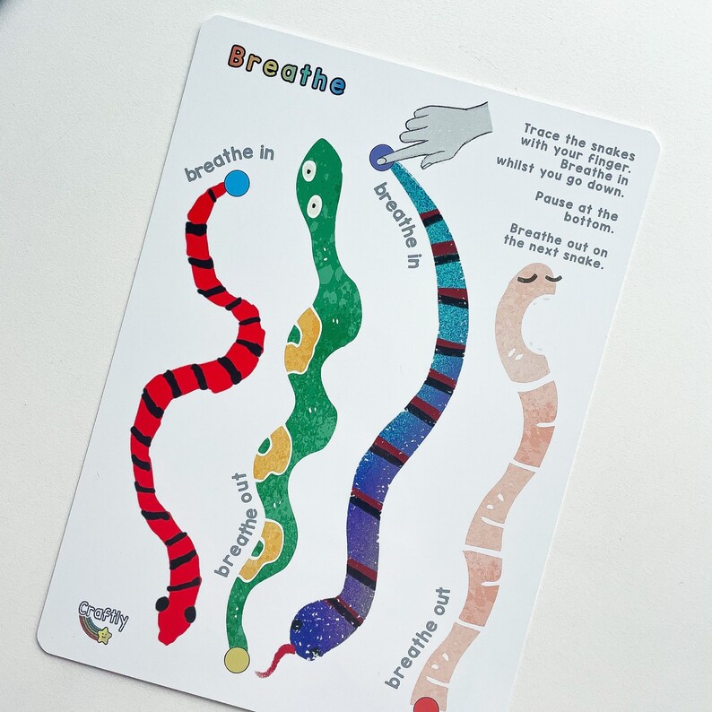 Puede incluir: Una tarjeta blanca con serpientes de colores sobre ella. La tarjeta tiene instrucciones para trazar las serpientes con el dedo mientras se respira. El texto en la tarjeta dice "Breathe", "breathe in", "breathe out", "Trace the snakes with your finger. Breathe in whilst you go down. Pause at the bottom. Breathe out on the next snake."