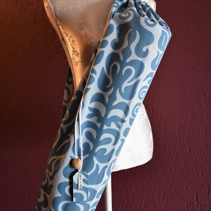 May include: A blue and white patterned yoga mat bag with a wooden toggle. The bag is hanging on a white mannequin.