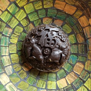 Puede incluir: Un quemador de incienso marrón oscuro con un diseño de mosaico. El quemador presenta una imagen tallada de dos peces y el carácter chino para "buena fortuna".