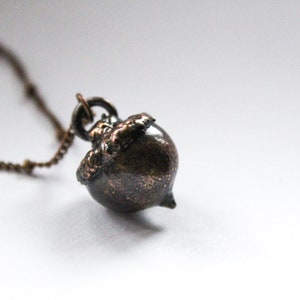 May include: A bronze acorn pendant necklace with a chain. The acorn is detailed with a textured surface and a small cap.