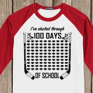 K&ouml;nnte beinhalten: Wei&szlig;es und rotes Baseball-T-Shirt mit schwarzem Text, der "Ich bin 100 Tage lang durch die Schule gelaufen" lautet. Das Design zeigt Hockeyschl&auml;ger und Pucks.