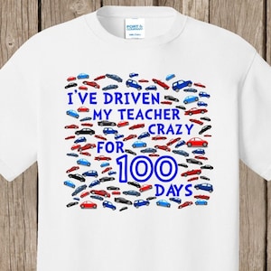 May include: White t-shirt with the text "I've driven my teacher crazy for 100 days" in blue. The design includes a collection of small car illustrations in red, blue, and black.
