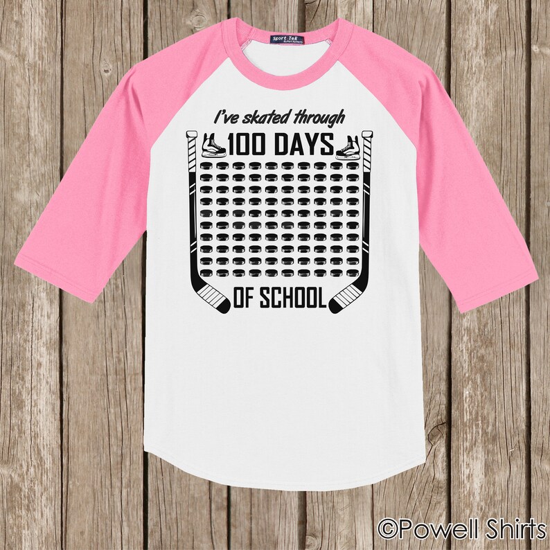 K&ouml;nnte beinhalten: Wei&szlig;es und rosafarbenes Baseball-T-Shirt mit schwarzem Text, der "Ich bin 100 Tage lang durch die Schule gelaufen" lautet. Der Text ist von einem Hockey-Schl&auml;ger- und Puck-Design umgeben.
