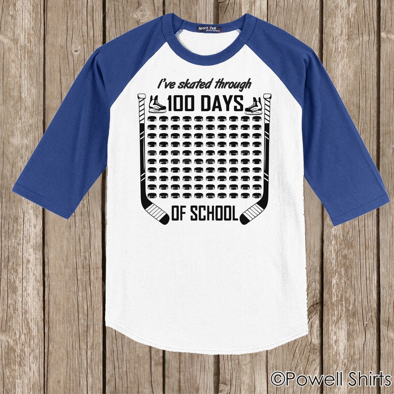 K&ouml;nnte beinhalten: Wei&szlig;es und blaues Baseball-T-Shirt mit einem Hockey-Puck-Design. Das Shirt sagt "Ich bin 100 Tage lang durch die Schule gelaufen".