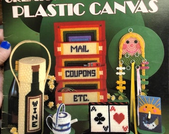 Könnte beinhalten: Ein Buchcover mit dem Titel "Kreative Projekte für Plastik-Canvas". Das Cover zeigt farbenfrohe Plastik-Canvas-Projekte, darunter eine Weinflasche, eine Teekanne, eine Taschentuchbox und ein Briefkasten-Organizer.