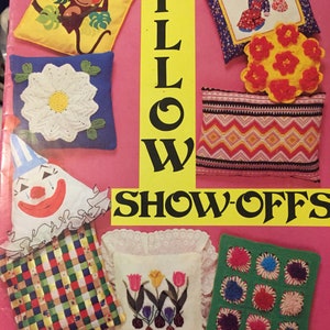 Puede incluir: Una colección de diseños de almohadas coloridos con varios temas, que incluyen un mono, una flor, un payaso, un patrón geométrico, tulipanes y un diseño de crochet. El título "PILLOW SHOW-OFFS" está impreso en la portada del libro.