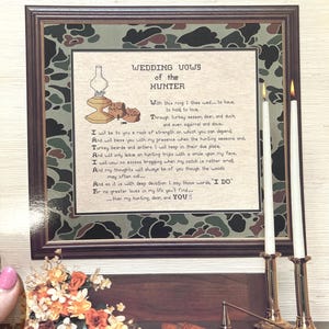 May include: A framed print of wedding vows for a hunter, with a green camouflage background. The vows are written in a traditional style and include references to hunting, deer, and duck. The print is titled "Wedding Vows of the Hunter" and is signed by Anne Henry.