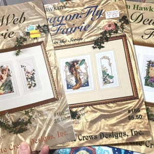 Könnte beinhalten: Drei Kreuzstichmuster mit Feen. Die Muster sind betitelt mit "Spider Web Fairie", "Dragon Fly Fairie" und "Dew Drop Fairie". Jedes Muster enthält ein gerahmtes Bild einer Fee mit einem Preisschild von 5,50 €.