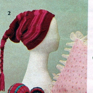 Può includere: Un cappello di lana rosa e rosso con una lunga treccia che pende dalla parte posteriore. Il cappello è su una testa di manichino bianca.