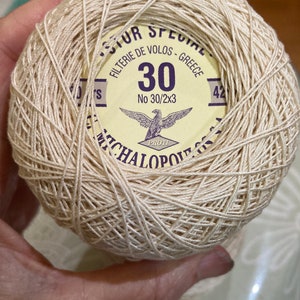 Könnte beinhalten: Eine Spule beigefarbener Stickgarn mit einem gelben Etikett, auf dem "SUR SPECIAL FILTERIE DE VOLOS - GREECE 30 No 30/2x3 PROTI MICHALOPOULOS 42" steht.