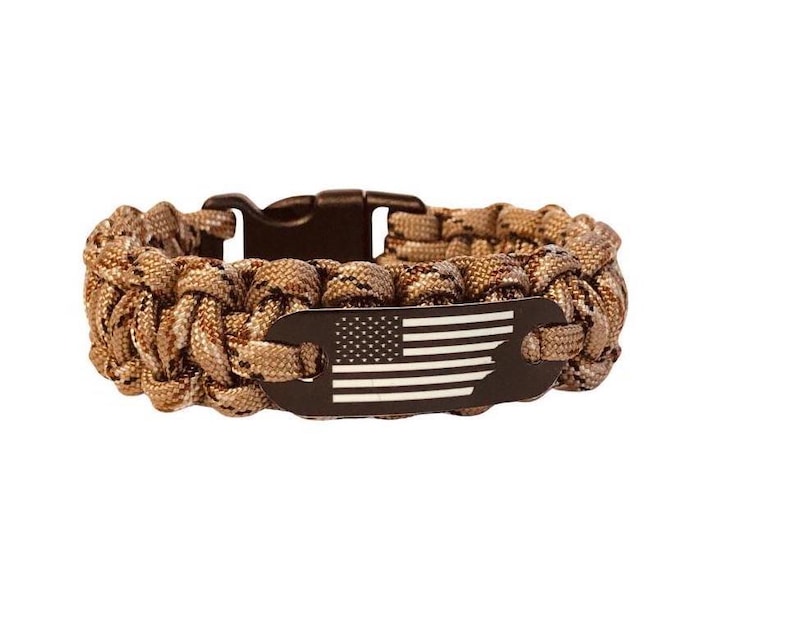 May include: A brown camouflage paracord bracelet with a black metal tag featuring a white American flag.