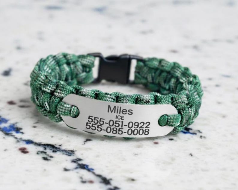 May include: A green and white paracord bracelet featuring a silver-toned metal identification plate engraved with the name Miles, the acronym ICE, and two phone numbers: 555-051-0922 and 555-085-0008, secured with a black plastic side-release buckle.