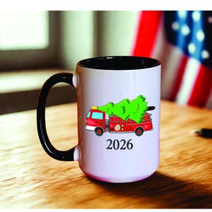 May include: A white ceramic mug with a black handle and the text "But First, Coffee" in a bold, black font. The mug is set against a blurred background, suggesting a cozy setting.