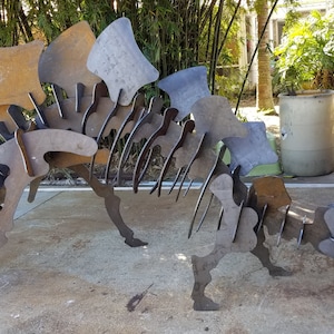 May include: A metal dinosaur sculpture made of flat pieces of metal. The sculpture is rusty in color and is standing on a concrete surface.