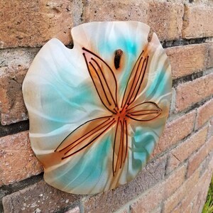 Pu&ograve; includere: Un'appendice murale decorativa a forma di dollaro di sabbia con sfondo verde acqua e bianco e un design a stella marina marrone.