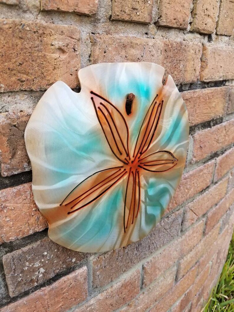 Pu&ograve; includere: Un'appendice murale decorativa a forma di dollaro di sabbia con sfondo verde acqua e bianco e un design a stella marina marrone.