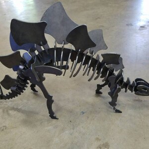 May include: A metal dinosaur skeleton sculpture with a large, spiky back. The sculpture is made of individual pieces of metal that are welded together.