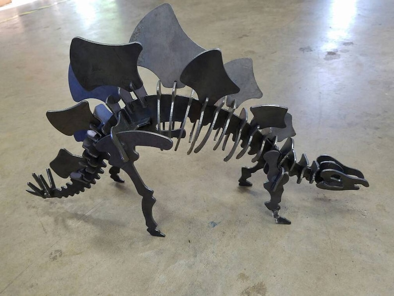 May include: A metal dinosaur skeleton sculpture with a large, spiky back. The sculpture is made of individual pieces of metal that are welded together.