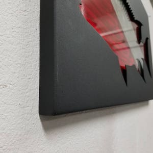 Puede incluir: Una pieza de arte de pared de metal negro con un dise&ntilde;o rojo y blanco cortado en forma de aleta de tibur&oacute;n.