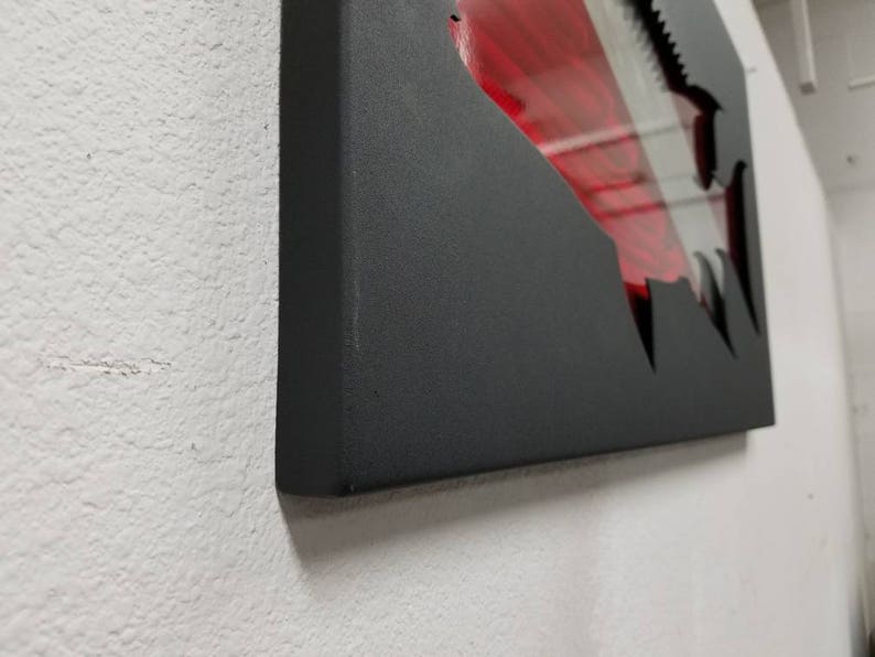 Puede incluir: Una pieza de arte de pared de metal negro con un dise&ntilde;o rojo y blanco cortado en forma de aleta de tibur&oacute;n.