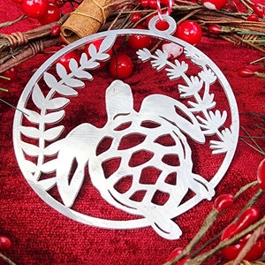 May include: A silver metal Christmas ornament shaped like a turtle with a leafy design around it.