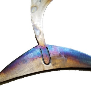 May include: Close-up of a metal fish tail sculpture with a rainbow iridescent finish. The tail is curved and has a small hole in the center.