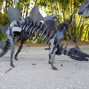 May include: A metal sculpture of a dinosaur skeleton with a large, spiky back. The sculpture is made of individual pieces of metal that are welded together. The dinosaur is standing on a concrete surface.