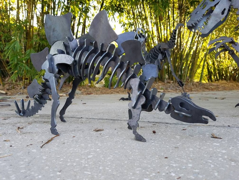 May include: A metal sculpture of a dinosaur skeleton with a large, spiky back. The sculpture is made of individual pieces of metal that are welded together. The dinosaur is standing on a concrete surface.