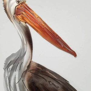 Puede incluir: Una escultura de metal de un pel&iacute;cano con un acabado marr&oacute;n y plateado. El pico del pel&iacute;cano es naranja y tiene un dise&ntilde;o detallado.
