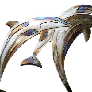May include: Metal wall art sculpture of three dolphins jumping out of the water. The dolphins are made of brushed metal with a rainbow iridescent finish.