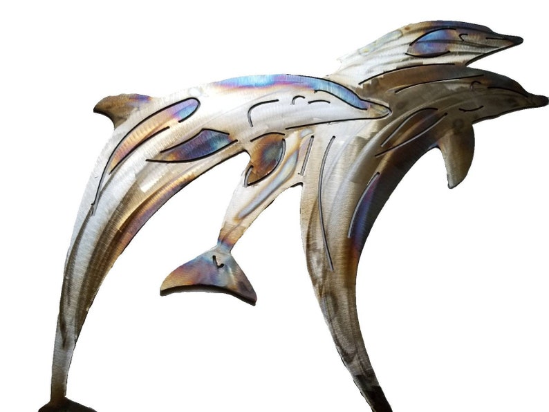 May include: Metal wall art sculpture of three dolphins jumping out of the water. The dolphins are made of brushed metal with a rainbow iridescent finish.