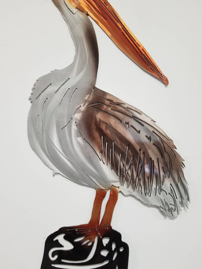 Puede incluir: Escultura de pared de metal de un pel&iacute;cano de pie sobre una roca. El pel&iacute;cano es gris con marcas marrones y tiene un pico naranja. La roca es negra.