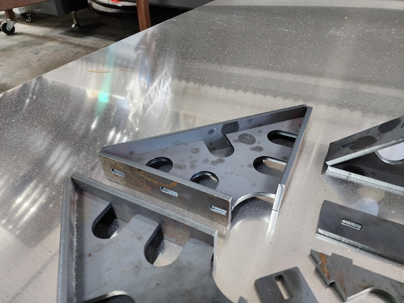 May include: Close-up of several metal brackets with cutouts. The brackets are arranged on a silver surface.